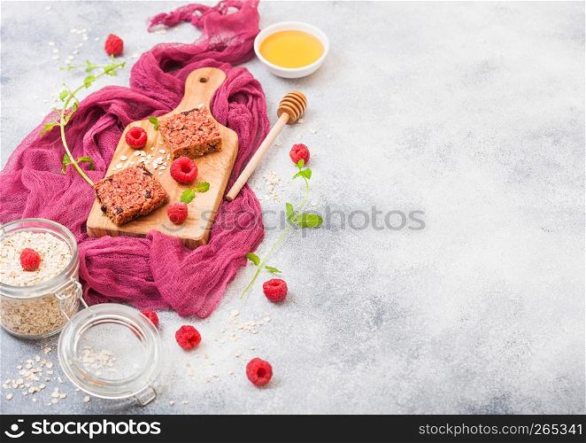 Organic cereal fruit granola bar with berries on vintage board with honey spoon and jar of oats on purple cloth. Strawberry, raspberry and blueberry with mint leaf and bowl of honey. Top view