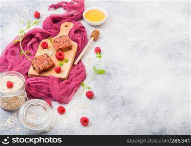 Organic cereal fruit granola bar with berries on vintage board with honey spoon and jar of oats on purple cloth. Strawberry, raspberry and blueberry with mint leaf and bowl of honey. Top view