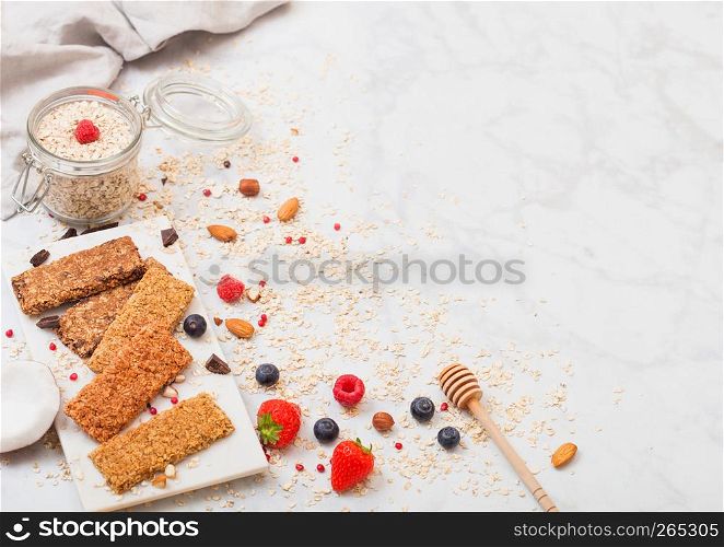 Organic cereal granola bar with berries on marble board with honey spoon and jar of oats and linen towel on marble background.