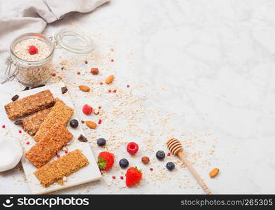 Organic cereal granola bar with berries on marble board with honey spoon and jar of oats and linen towel on marble background.