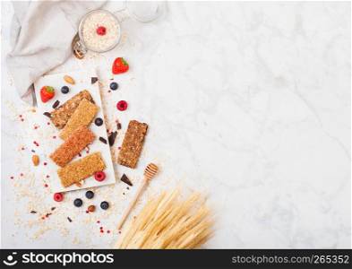 Organic cereal granola bar with berries on marble board with honey spoon and jar of oats and linen towel on marble background.