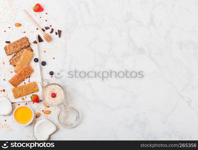 Organic cereal granola bar with berries on marble board with honey spoon and jar of oats and coconut on marble table background.