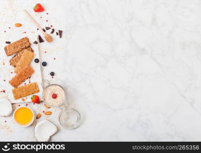 Organic cereal granola bar with berries on marble board with honey spoon and jar of oats and coconut on marble table background.