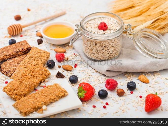 Organic cereal granola bar with berries on marble board with honey spoon and jar of oats and linen towel on marble table background.