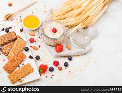 Organic cereal granola bar with berries on marble board with honey spoon and jar of oats and linen towel on marble table background.