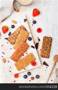 Organic cereal granola bar with berries on marble board with honey spoon and jar of oats and linen towel on marble table background.