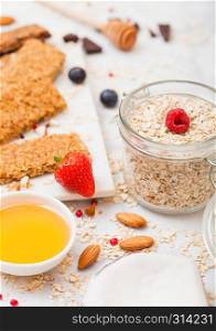 Organic cereal granola bar with berries on marble board with honey spoon and jar of oats and coconut on marble table background.