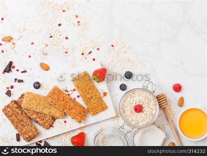 Organic cereal granola bar with berries on marble board with honey spoon and jar of oats and coconut on marble table background.