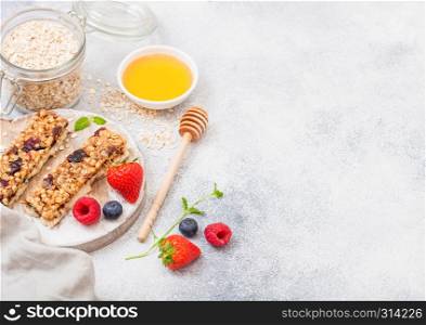 Organic cereal granola bar with berries on round vintage board with honey spoon and jar of oats on marble background. Strawberry, raspberry and blueberry with mint leaf