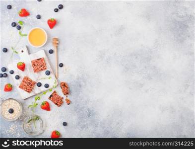 Organic cereal granola bar with berries on vintage board with honey spoon and jar of oats on marble background. Strawberry, raspberry and blueberry with mint leaf