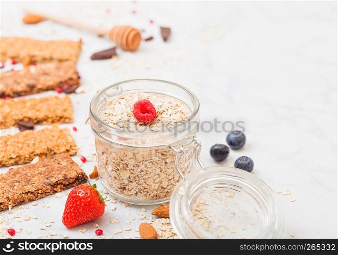 Organic cereal granola bar with berries with honey spoon and jar of oats on marble table background.Top view. Strawberry, raspberry and blueberry with almond nuts.
