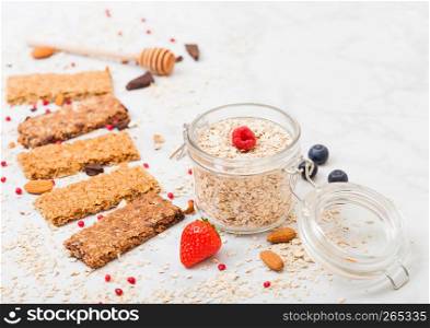 Organic cereal granola bar with berries with honey spoon and jar of oats on marble table background.Top view. Strawberry, raspberry and blueberry with almond nuts.
