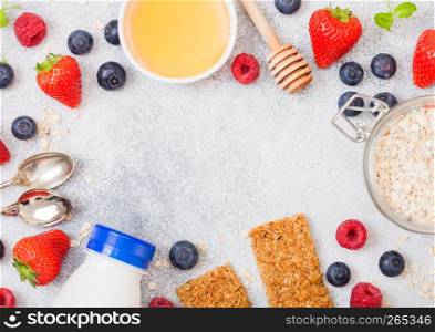 Organic cereal granola bar with berries with honey spoon and jar of oats and bottle of milk drink on stone background. Top view. Strawberry, raspberry and blueberry with almond nuts.