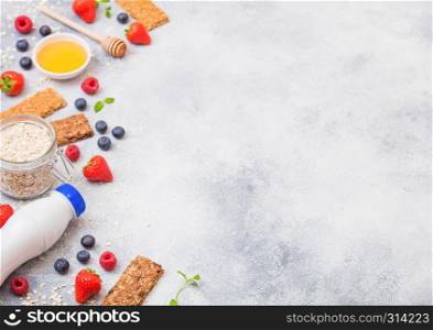 Organic cereal granola bar with berries with honey spoon and jar of oats and bottle of milk drink on stone background. Top view. Strawberry, raspberry and blueberry with almond nuts.