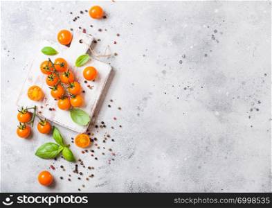 Organic Cherry Orange Rapture Tomatoes on the Vine with basil and pepper on chopping board on stone background.