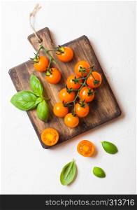 Organic Cherry Orange Rapture Tomatoes on the Vine with basil on chopping board on white background.