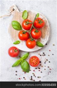 Organic Cherry Tomatoes on the Vine with basil and pepper on chopping board on stone background.