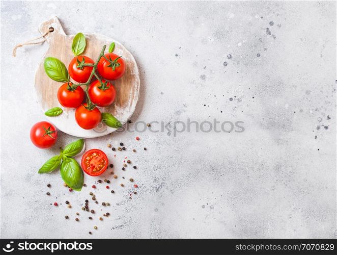 Organic Cherry Tomatoes on the Vine with basil and pepper on chopping board on stone background.