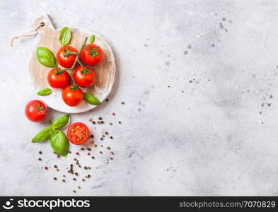 Organic Cherry Tomatoes on the Vine with basil and pepper on chopping board on stone background.