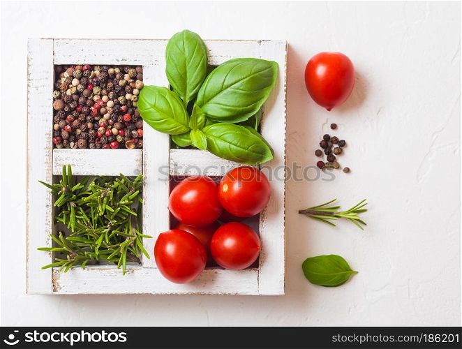 Organic Cherry Tomatoes with basil and pepper and rosemary in white wooden box on stone background.