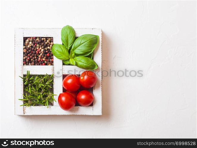 Organic Cherry Tomatoes with basil and pepper and rosemary in white wooden box on stone background.