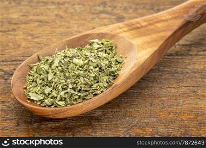 organic dried oregano leaf on a wooden spoon against a grunge wood background