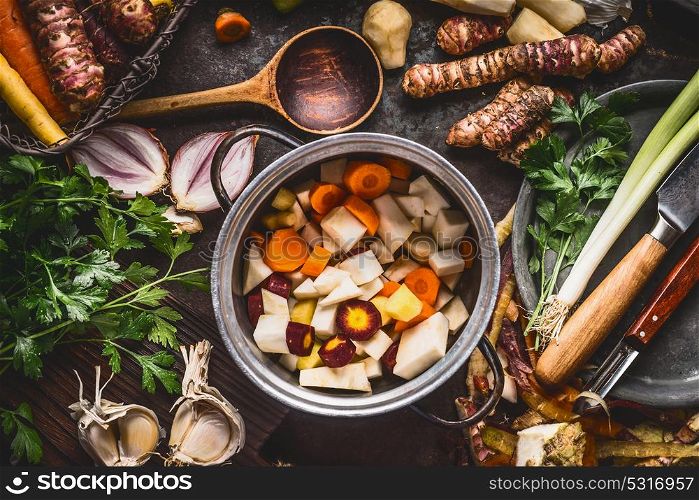 Organic farm vegetables cooking and eating. Cooking pot with diced colorful root vegetables on rustic kitchen tables background with spoon and ingredients. Healthy clean food concept