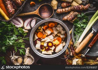 Organic farm vegetables cooking and eating. Cooking pot with diced colorful root vegetables on rustic kitchen tables background with spoon and ingredients. Healthy clean food concept