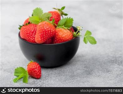Organic fresh raw strawberries with leaf in black ceramic bowl on light table background. Top view