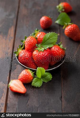 Organic fresh raw strawberries with leaf in steel bowl on wooden table background.