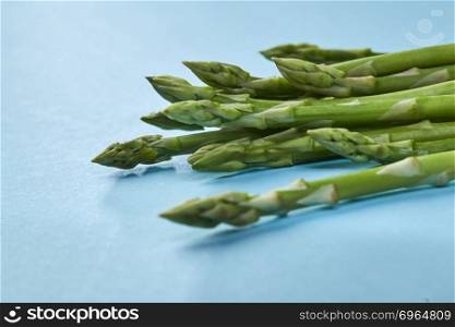 Organic green asparagus in a bunch ready to cook healthy vegetarian food on blue background.. Sprigs of green asparagus in a bunch on a blue background for cooking healthy food.