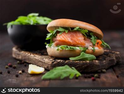 Organic healthy sandwich with salmon and bagel, cream cheese and wild rocket on wooden board with lemon and pepper.