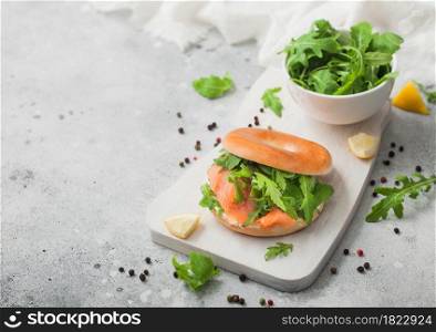 Organic healthy sandwich with salmon and bagel, cream cheese and wild rocket on light kitchen table.