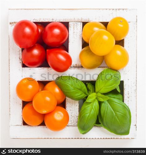 Organic Mini Tomatoes with basil and pepper in wooden box on stone kitchen background.