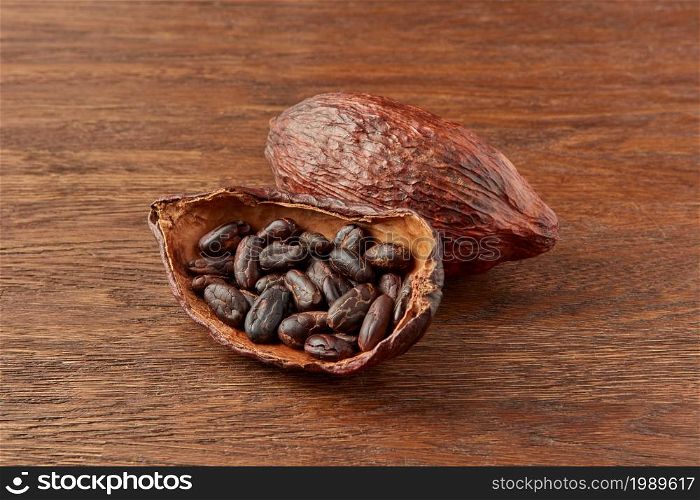Organic natural pod of cocoa tree filled with brown cocoa beans placed on wooden background. Halved pod with cocoa beans