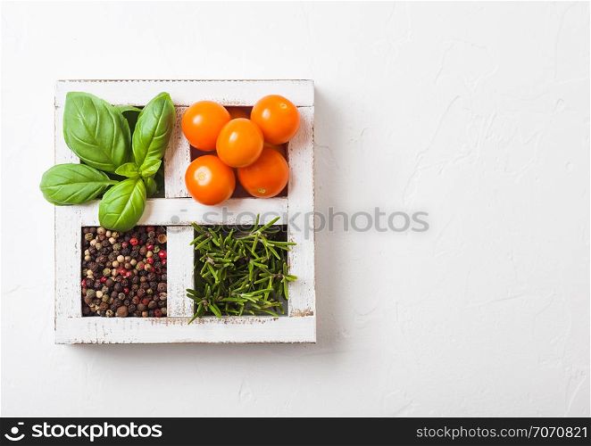 Organic Orange Rapture Cherry with basil and pepper and rosemary in white wooden box on stone kitchen background.