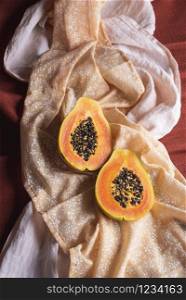 Organic papaya fruit, cut in halves, on orange fabric background. Above view of ripe tropical fruit. Tasty summer fruit. Papaya halves with seeds.