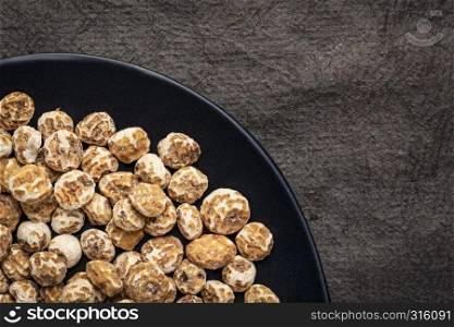 organic peeled tiger nuts, a rich source of resistant starch, top view on a black plate against textured bark paper