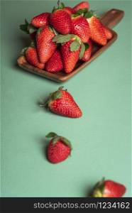 Organic ripe strawberries on wooden platter on green table. Tasty red berries on aqua menthe background. Sweet summer fruits. Strawberry fruits pile.