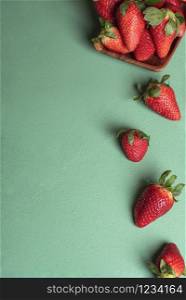 Organic strawberries fallen from a wooden plate on a green table. Fresh strawberry fruits. Berries harvest. Sweet summer fruits. Popular red fruits.