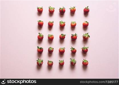 Organic strawberry fruits arranged in rows with equal distance between them. Fresh strawberries aligned on a pink table, above view.