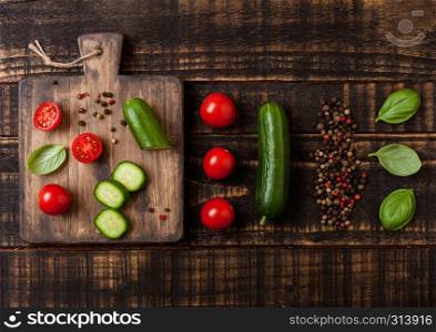 Organic Tomatoes and cucumbers with basil and linen towel on chopping board on wooden kitchen table.