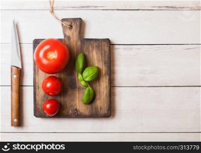 Organic Tomatoes with basil on chopping board with knife on wooden table.