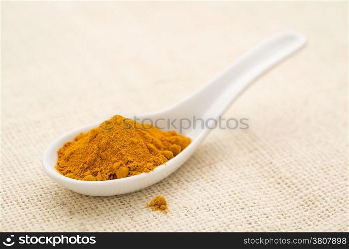 organic turmeric root powder on a white Chinese spoon against burlap canvas