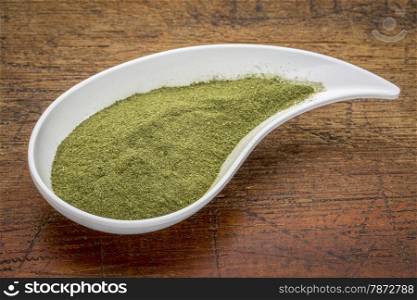 organic wheatgrass powder on a white teardrop shaped bowl against rustic wood