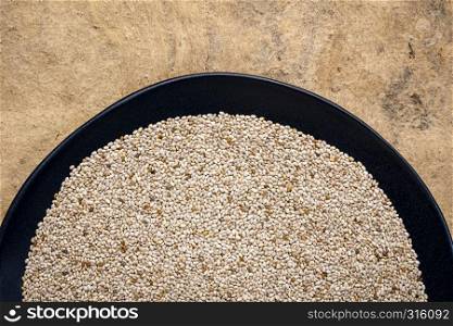 organic white chia seeds rich in omega-3 fatty acids, top view of a black plate against textured bark paper