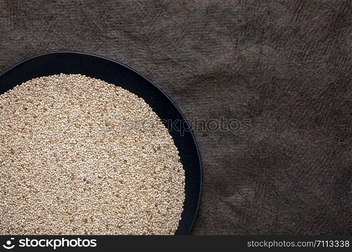 organic white chia seeds rich in omega-3 fatty acids, top view of a black plate against textured bark paper with a copy space