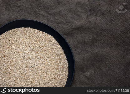 organic white chia seeds rich in omega-3 fatty acids, top view of a black plate against textured bark paper with a copy space