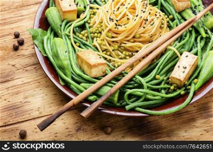 Oriental salad with pasta, asparagus beans,fried cheese and okra on wooden table. Oriental vegetable salad with pasta