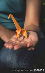 Origami orange color giraffe on hand.